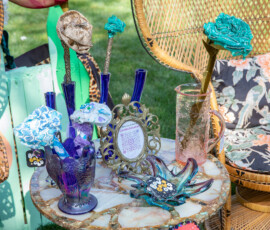 Cobalt blue bud vases holding fabric roses beside a carnival glass bird vase and blown glass dish on a vintage table at the Beverly Garden Party