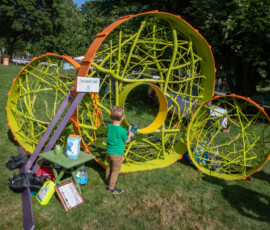 A young boy blows bubbles inside Trois Dandy Lions, a large lime-green sculpture of painted branches formed into three spheres on Beverly Common