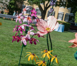 Painted metal garden sculpture of pink cosmos, purple orchids and black-eyed Susans standing on the lawn of Beverly Common