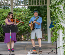 Wider view of the violin and guitar duo performing in the vine-covered gazebo during Beverly's Garden Party