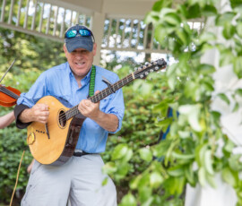 A musician plays a round-backed guitar while a violinist accompanies him in the gazebo at Beverly's Garden Party