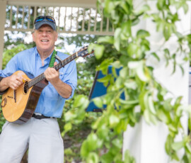 A guitarist performs beneath the gazebo roof on Beverly Common, seen through hanging vines at the Beverly Garden Party