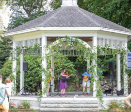 Musicians perform in the vine-draped white gazebo on Beverly Common as a small crowd listens on the grass at the Beverly Garden Party