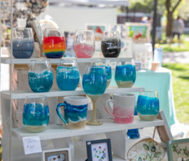 Stemless wine glasses and mugs finished with blue and teal resin waves, displayed on a tiered stand at Beverly's Garden Party