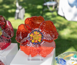 Fused glass poppy sculptures in deep red and orange displayed on white pedestals at a maker booth on Beverly Common
