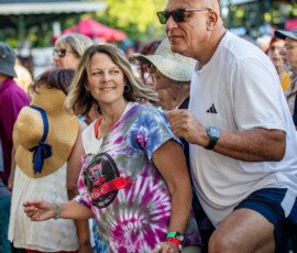 A group gathers outdoors at the Salem Jazz and Soul Festival 2026 in Salem Willows. Some smile in casual summer clothes; a woman in a tie-dye shirt and a man in sunglasses stand out amid trees and fellow festival-goers enjoying the lively scene.