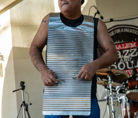 A man in a sleeveless shirt and jeans plays a large washboard with metal finger picks on stage at the 2026 Salem Jazz and Soul Festival, held at Salem Willows. Drums, a mic stand, tent, and festival banner appear in the background.